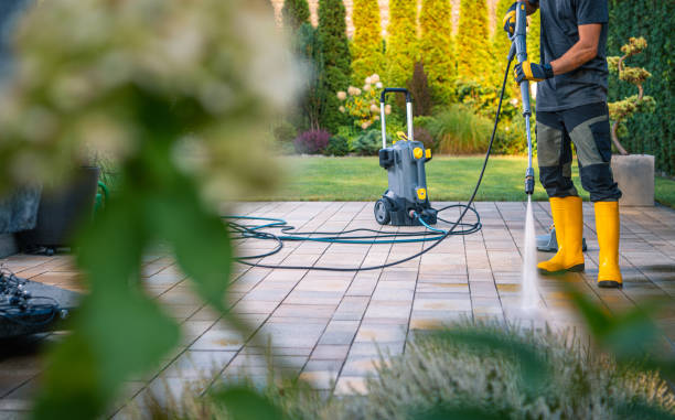 Man uses an electric pressure washer to clean a dirty outdoor patio.