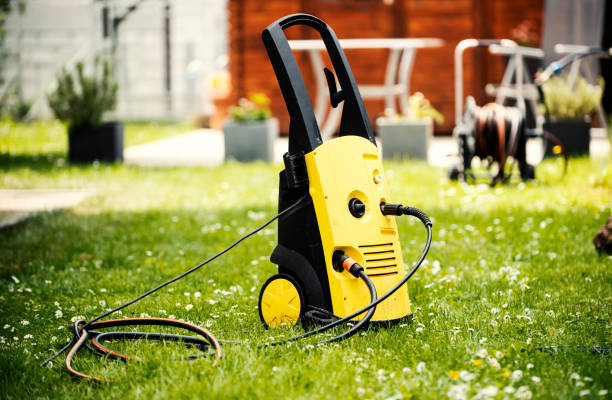 Yellow electric pressure washer with hoses lying on a green lawn.