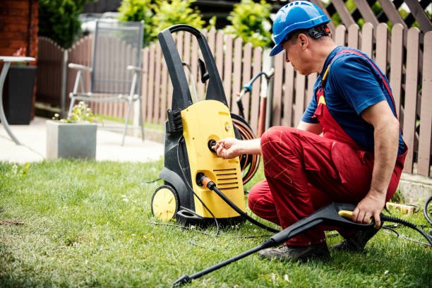 Man connecting hose to an electric pressure washer on a grassy backyard.