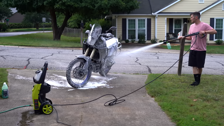 Man uses an electric pressure washer to thoroughly clean his dirty motorcycle.