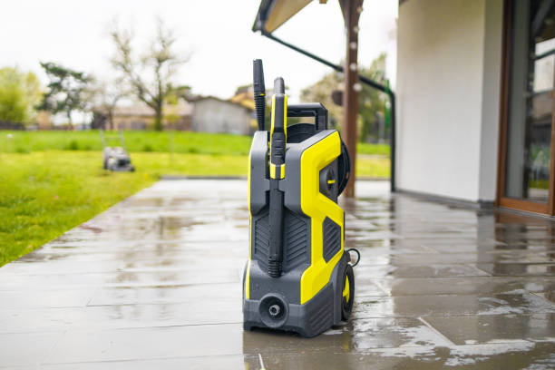 Bright yellow electric pressure washer standing on a wet paved patio.