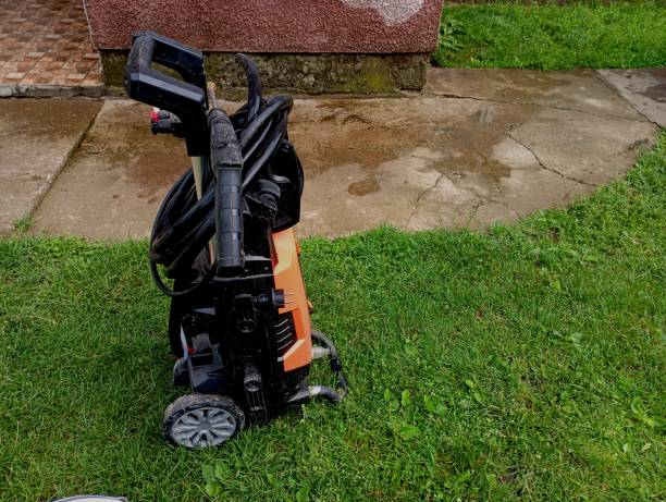 Orange and black electric pressure washer with wheels and coiled hose on grass.