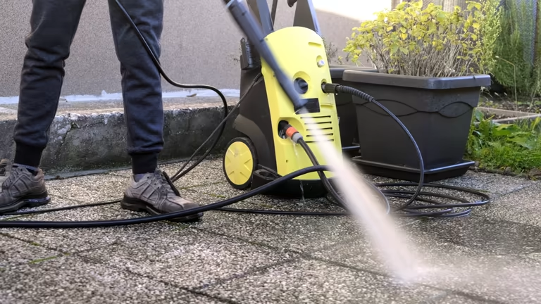 Person using a yellow electric pressure washer to clean outdoor patio tiles.