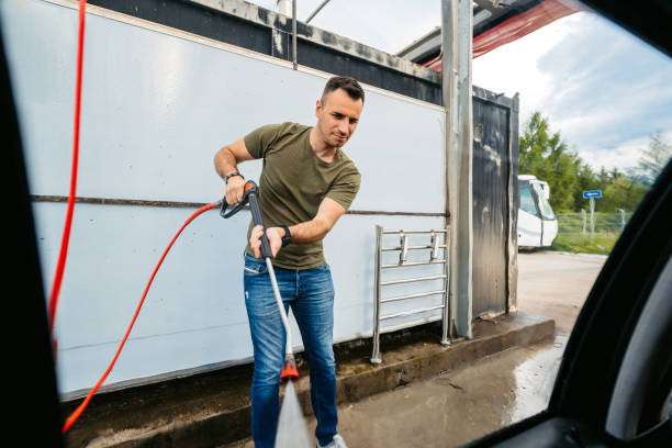 Man using an electric pressure washer to clean a vehicle at a car wash.