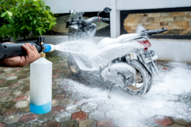 User cleaning motorcycle with foam from an electric pressure washer, effective cleaning solution.