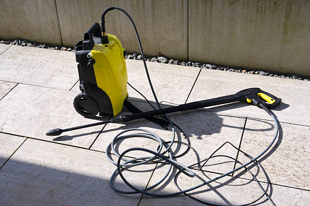 A yellow electric pressure washer machine with hose and spray gun on a patio.