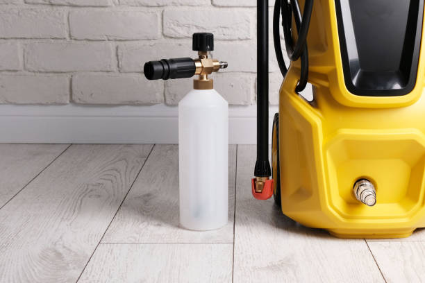 Yellow electric pressure washer with foam cannon attachment ready for use on wooden floor.