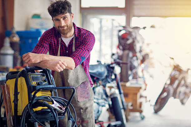 Smiling man in workshop; a powerful electric pressure washer cleans tools efficiently.