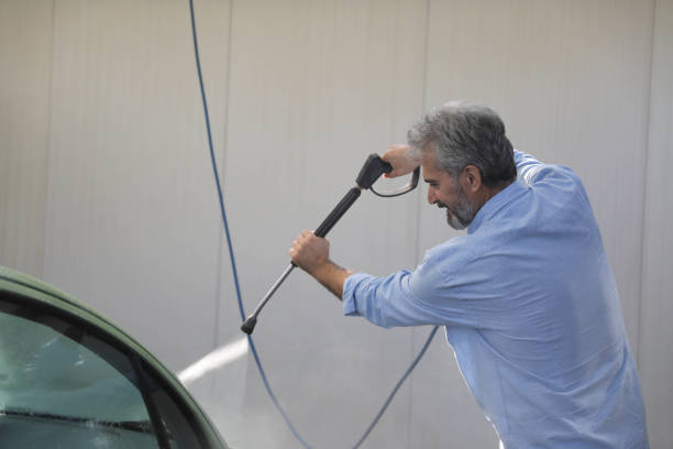 Man actively cleaning a car's windshield with an electric pressure washer at a wash.