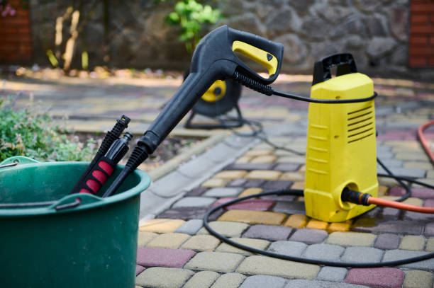 Outdoor electric pressure washer unit and spray gun resting in a green bucket on pavers.