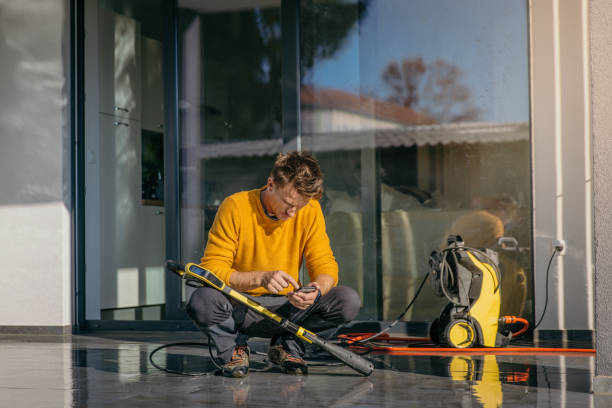 Man checking phone on clean patio next to yellow electric pressure washer.