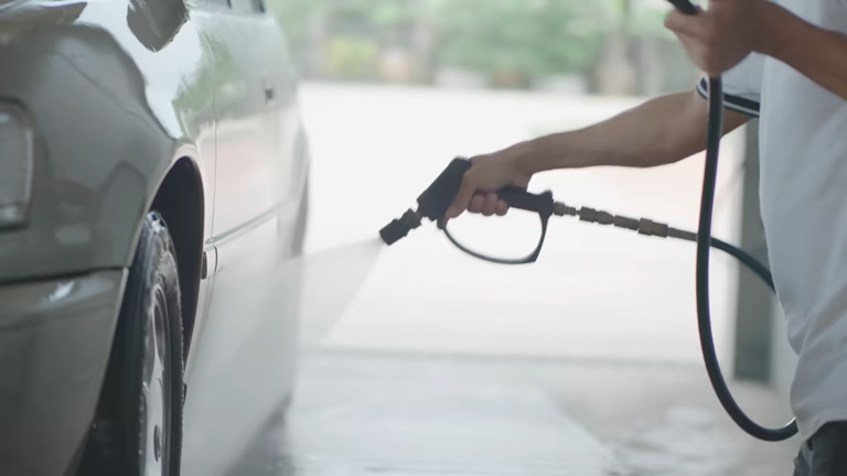 Close-up of an electric pressure washer nozzle spraying water onto a grey car.