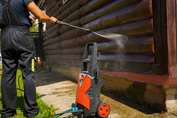 Cleaning a wooden log cabin wall with a powerful electric pressure washer.