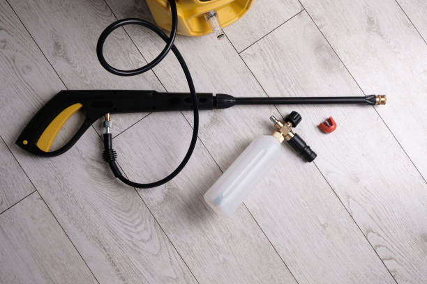Electric pressure washer gun, hose, and foam cannon bottle laid on a light wooden floor.