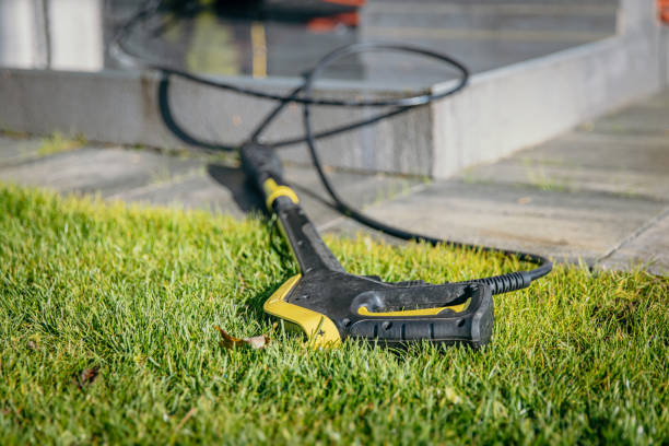 An electric pressure washer gun lies on the grass, ready for patio cleaning.