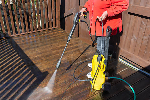 Person cleaning deck with electric pressure washer.